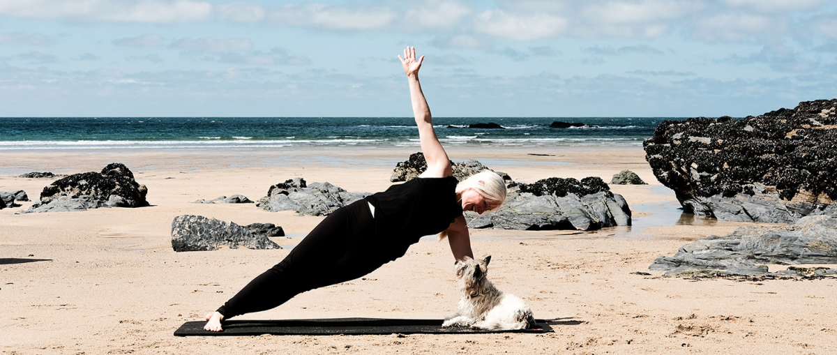Heidi doing a side plank on the beach whilst her dog Lola looks up to see if there is a treat in her hand!
